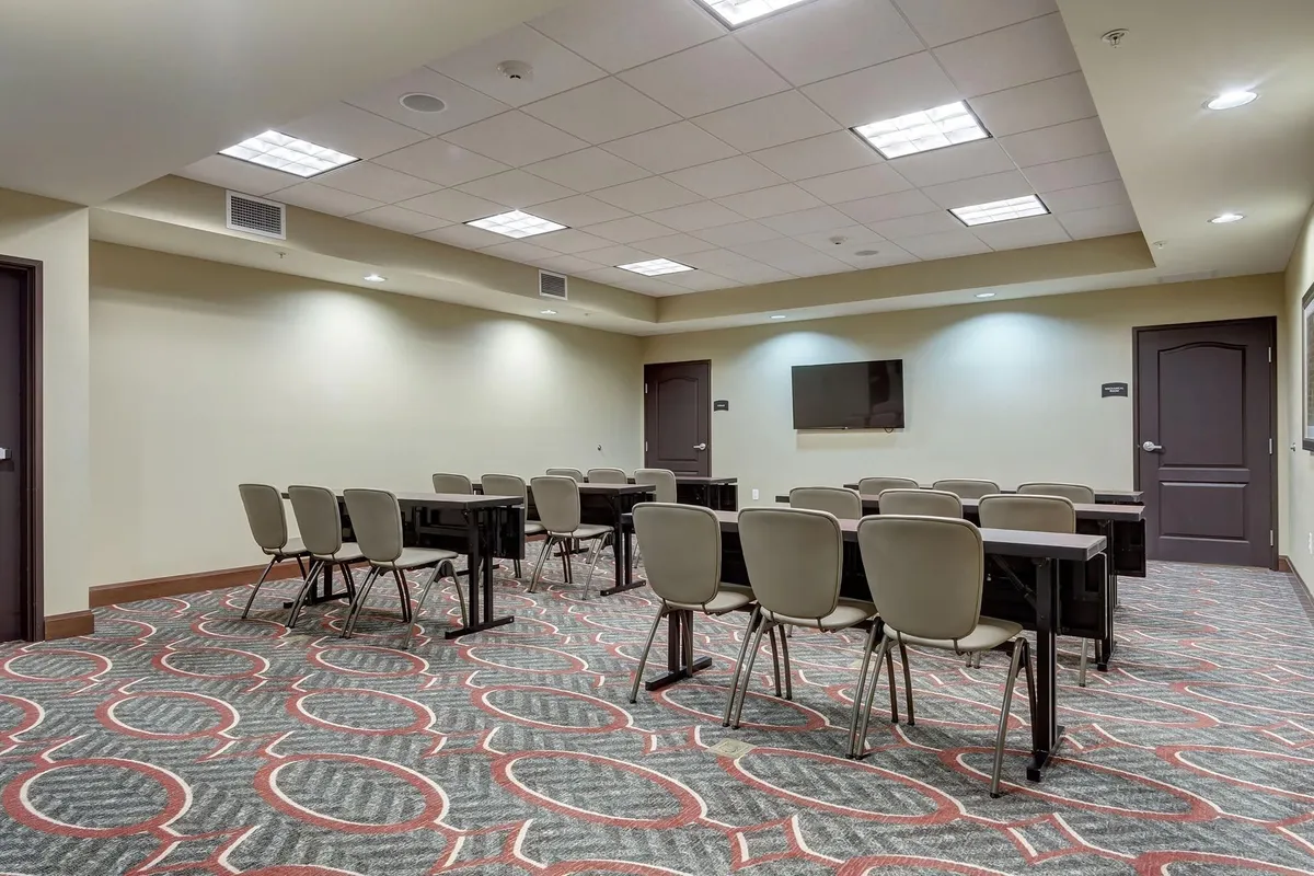 An inviting interior with tables and chairs arranged for collaborative activities, a prominent television, and patterned carpet underfoot. The setting is conducive to informal gatherings and group planning.