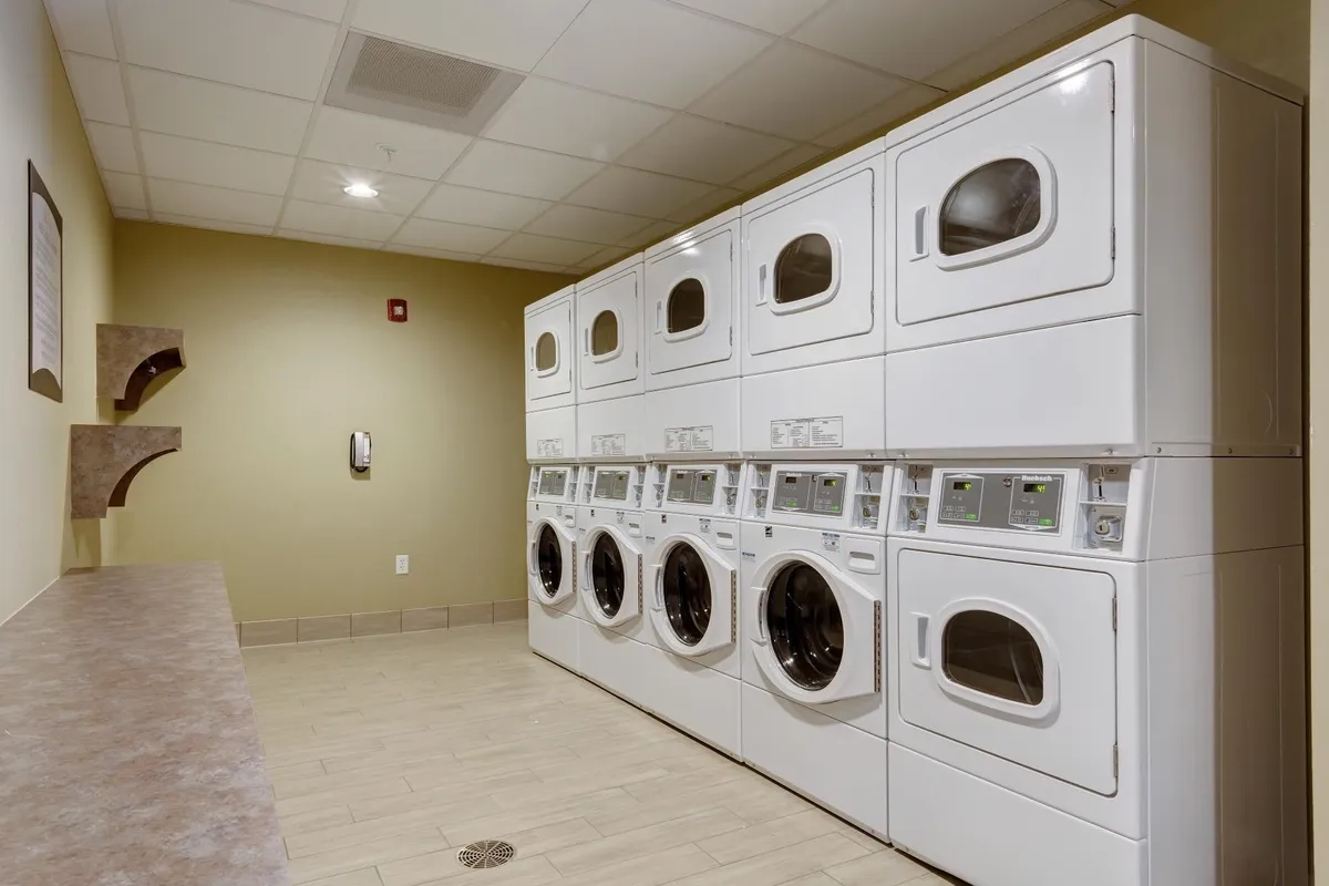 A practical laundry room with rows of modern washing machines and dryers, complemented by a countertop for folding clothes and tasteful wall décor. The ambiance is efficient yet comfortable, designed for extended-stay convenience and occasional guest interactions.