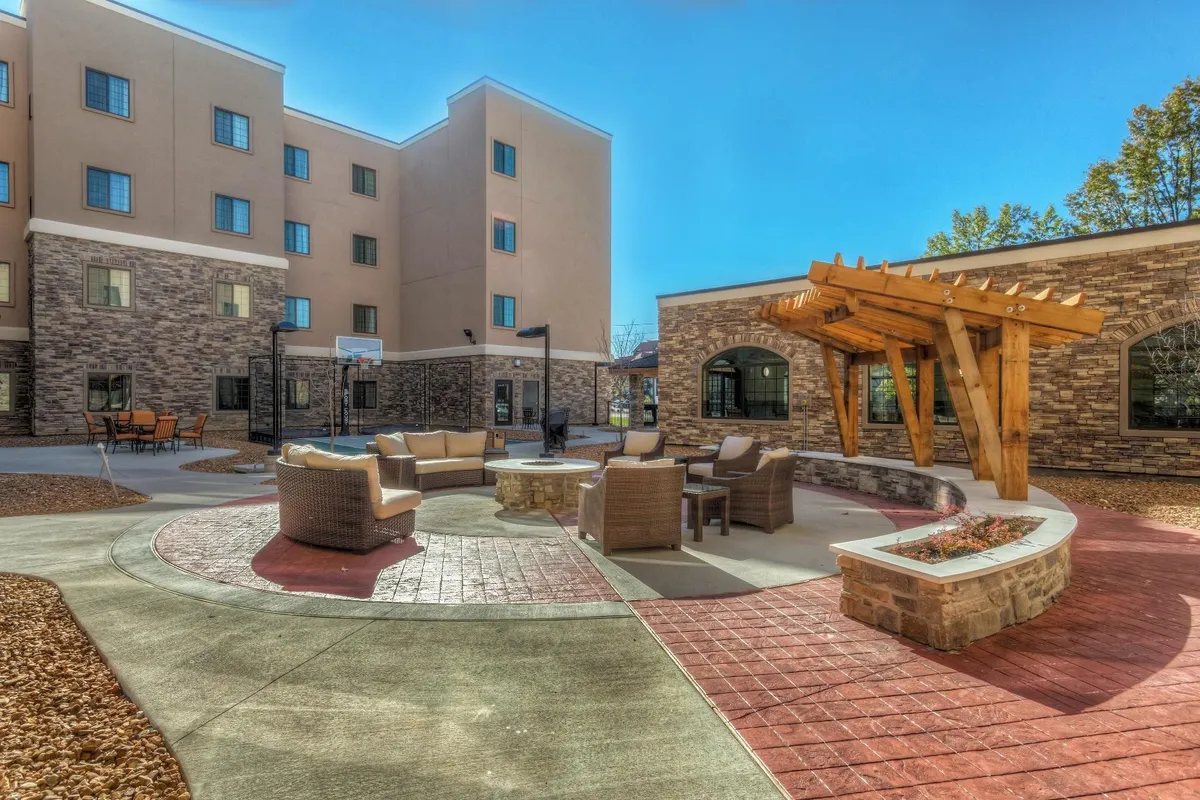 An inviting outdoor space at the hotel, featuring a cozy seating area, fire pit, pergola, and a glimpse of the building facade in the background. The scene suggests opportunities for families to relax together after a day of adventure, enjoy sunset views, or share meals outdoors in a communal, welcoming setting.