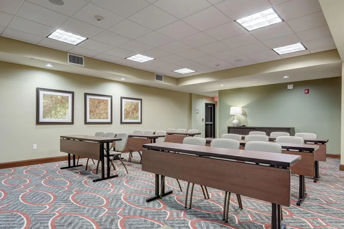 A well-lit interior space featuring tables arranged for group activities or meetings, adorned with framed artworks on the walls and illuminated by a side table lamp. The space exudes a welcoming, communal atmosphere designed for larger gatherings.