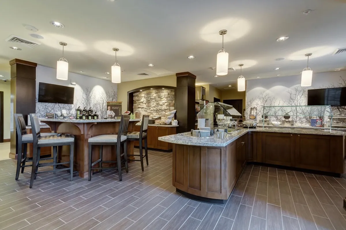 The central bar area, highlighted by a striking stone feature wall and a food display counter, is surrounded by seating that encourages casual dining and informal gatherings. The setting is modern, spacious, and ideal for both socializing and enjoying meals or drinks, easily adaptable for work or relaxation.
