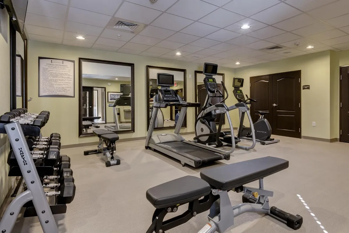 A well-equipped fitness center featuring a treadmill, elliptical machine, weight bench, dumbbells, and wall mirrors. The space is clean, modern, and designed for guests aiming to maintain their health and fitness routines during their stay.