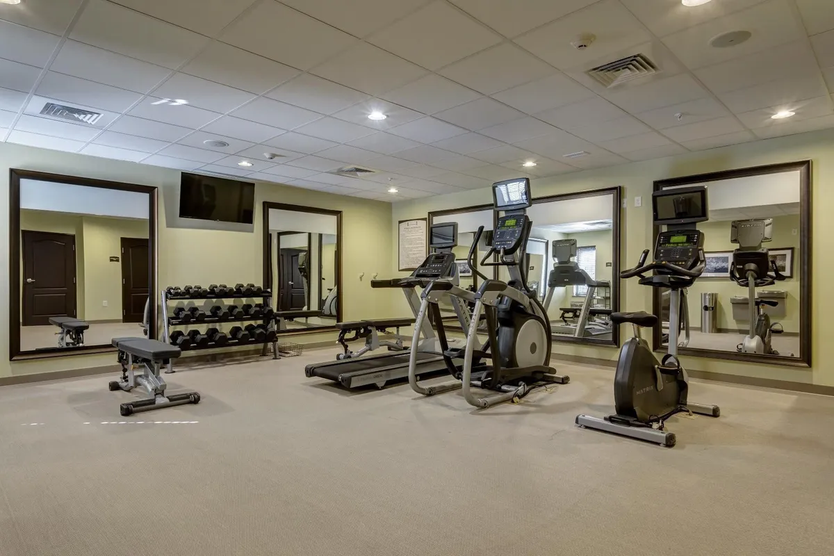 A well-equipped, modern fitness center featuring treadmills, ellipticals, a dumbbell rack, and large mirrors. The space is clean and organized, creating an energetic, motivational atmosphere for guests interested in fitness and healthy routines.